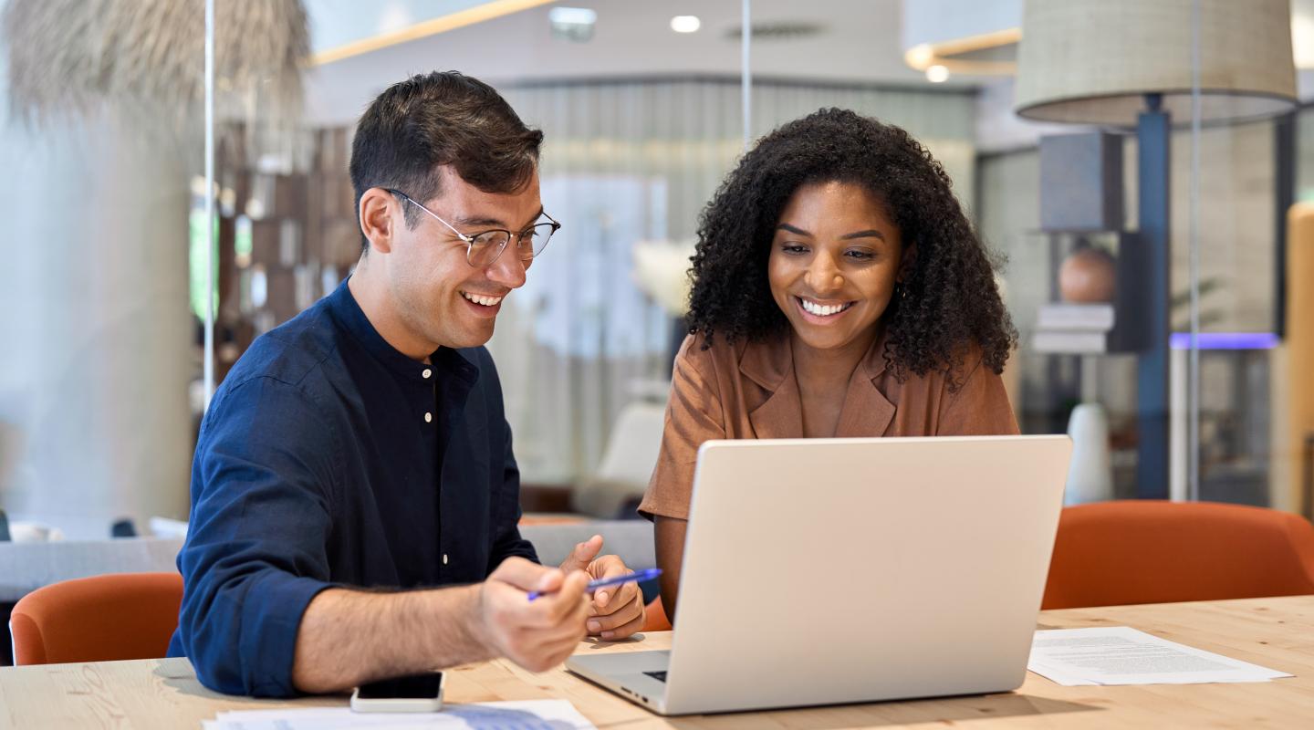 Male and female business professionals at an office desk looking at a laptop