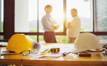 Contractors IBC MDS codes.jpeg Two contractors talking in front of a desk with construction items on it