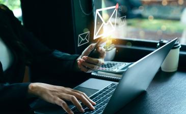business woman sitting at laptop holding her phone, email envelope graphic above phone