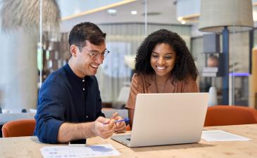 Male and female business professionals at an office desk looking at a laptop
