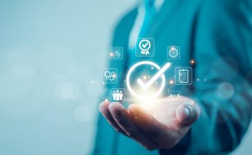 Torso of male in a suit, holding his hand palm outstretch. There are floating graphics of a checkmark, gears, documents and people in his hand.