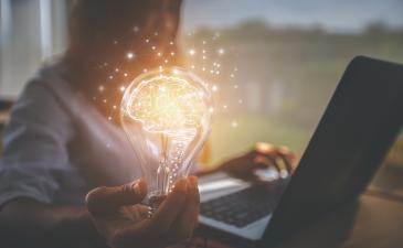Business woman working on a laptop and holding out a lightbulb with a brain icon inside