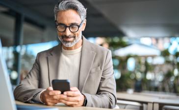 male professional with grey hair and glasses looking at his phone and smiling