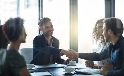 Business colleagues at a meeting shaking hands with a young man in a suit