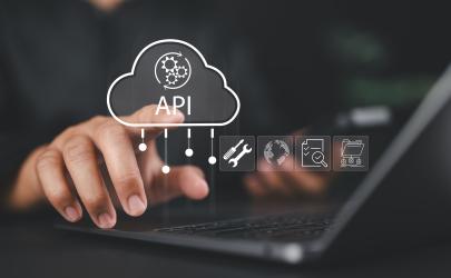 Male businessman sitting at a desk in front of his laptop pointing to a cloud graphic and the words 'API' in white