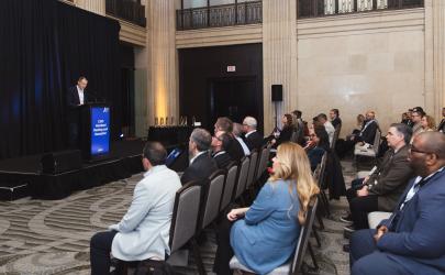 CSIO Board Chair Michael Lin speaking on a podium in front of members in a large banquet hall