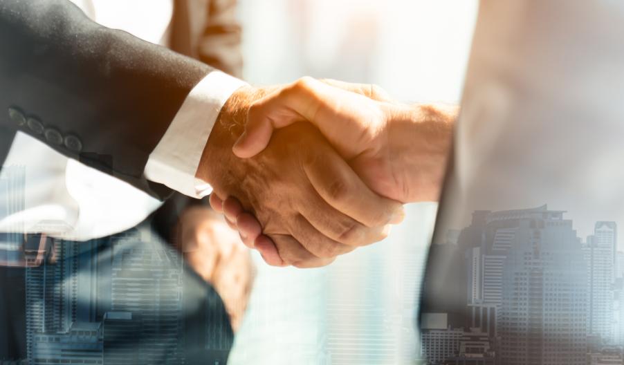 Close up of two businesspeople shaking hands with city skyline in the background