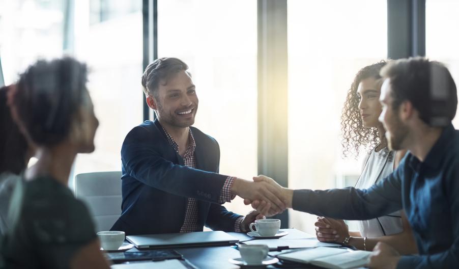 Business colleagues at a meeting shaking hands with a young man in a suit