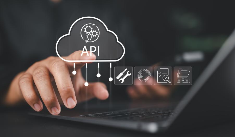 Male businessman sitting at a desk in front of his laptop pointing to a cloud graphic and the words 'API' in white